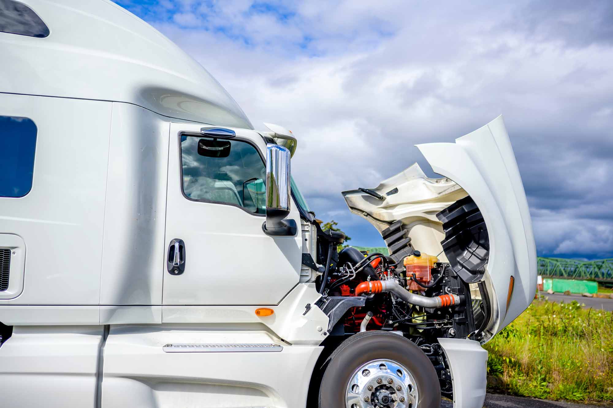 Broken Big rig industrial professional white semi truck with open hood and long haul semi trailer standing on the road shoulder trying to fix breakdown in place and waiting for road repair assistant